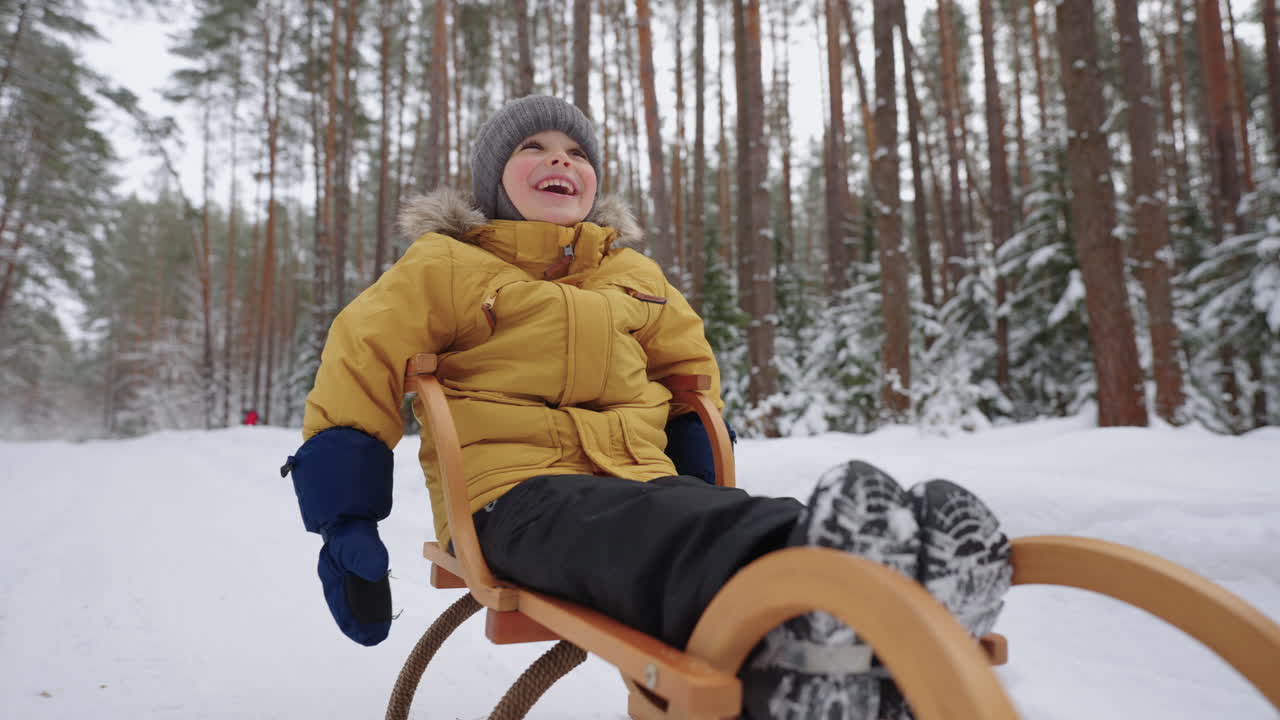Portrait of a smiling boy 3-4 years old in slow motion who rides a sled in a snowy forest in winter