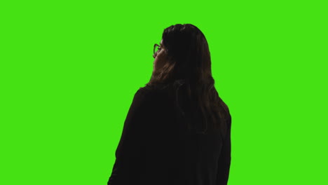 businesswoman holding blue screen mobile phone towards camera standing against green screen with low key lighting