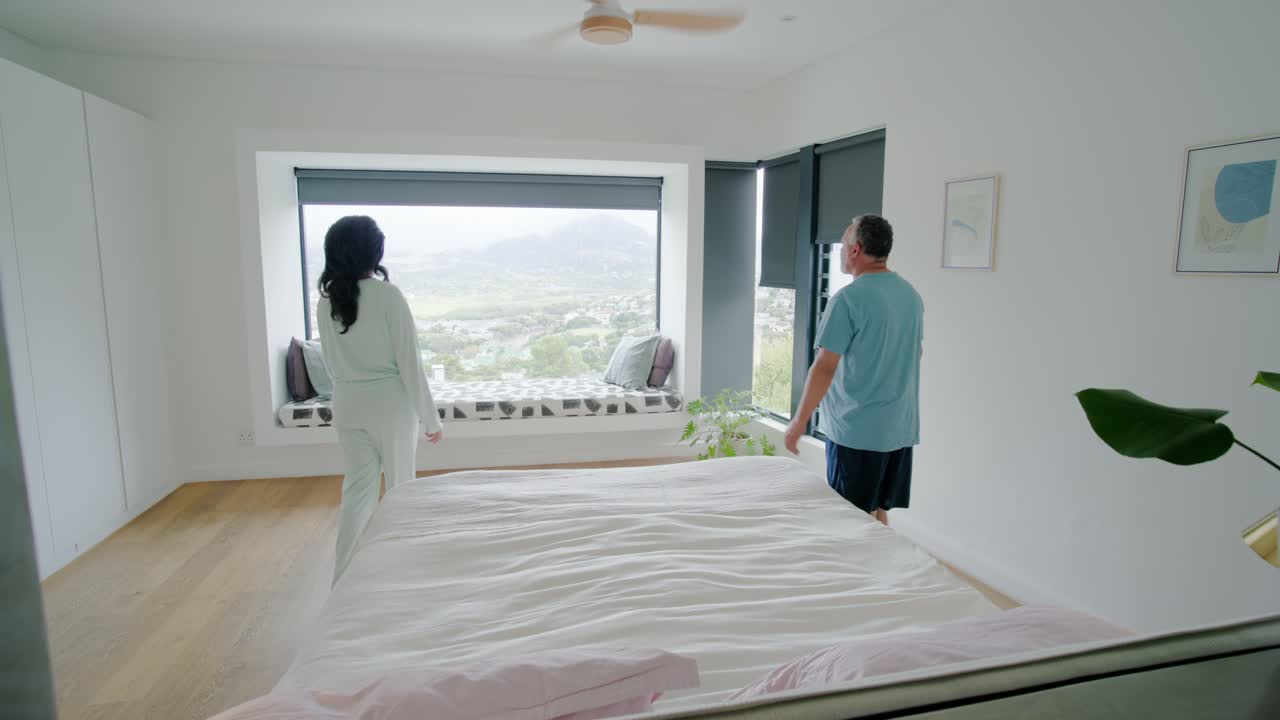 African American couple watching woman making bed with pink pillow walking window seat hugging view