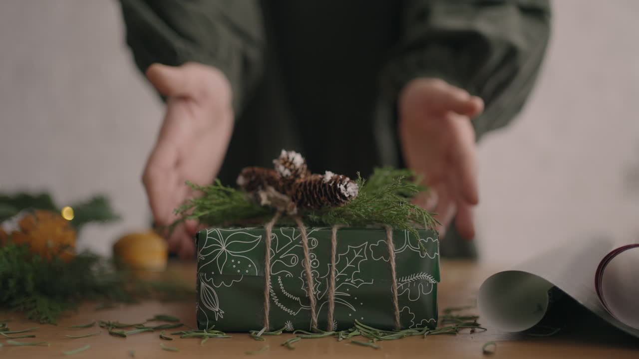 A Christmas present moves a woman's hands into the camera. green Packaged Gift Woman Moves Into Camera After Packing and Decorating. Slow motion
