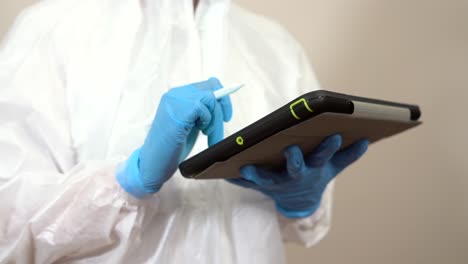 hands of female doctor with gloves and ppe suit using tablet to consult job information