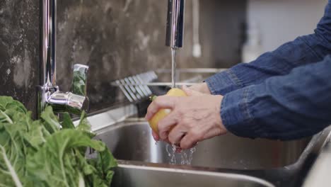 Midsection-of-senior-caucasian-woman-washing-yellow-pepper-in-kitchen-sink,-slow-motion