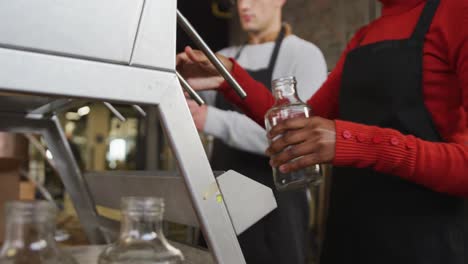 sección media de dos colegas diversos en la destilería de ginebra llenando y sujetando las tapas de las botellas a mano