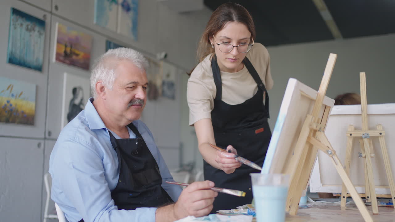 vista de ángulo alto de amigos mayores alegres pintando en lienzo. mujer mayor sonriendo mientras dibuja con el grupo. mayores asistiendo a clase de pintura juntos. hombres mayores divirtiéndose pintando en clase de arte