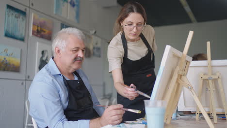 High-angle-view-of-cheerful-senior-friends-painting-on-canvas.-Senior-woman-smiling-while-drawing-with-the-group.-Seniors-Attending-Painting-Class-Together.-Senior-men-having-fun-painting-in-art-class