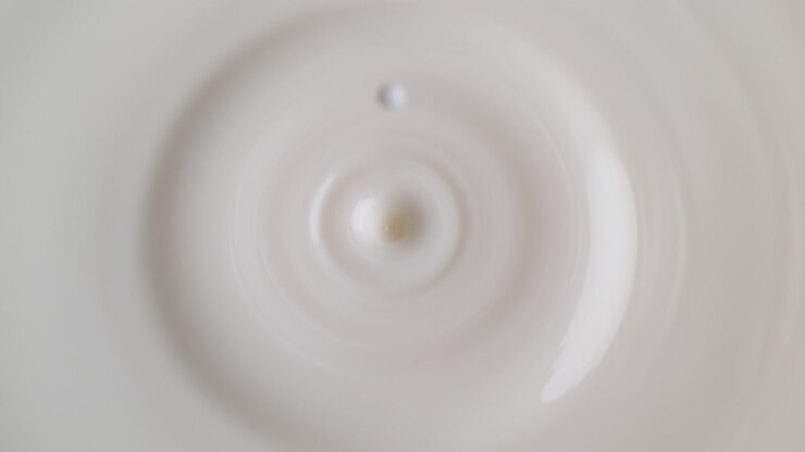 Milk Drop Dripping Onto The White Liquid Surface Making Splash Crown And Ripples in Macro and Slow Motion