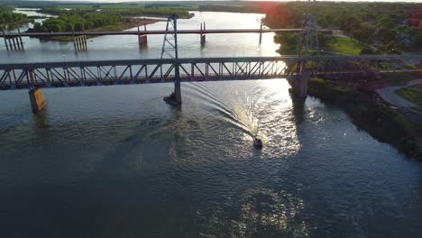 Boat-going-under-a-bridge-at-sunset-in-4K