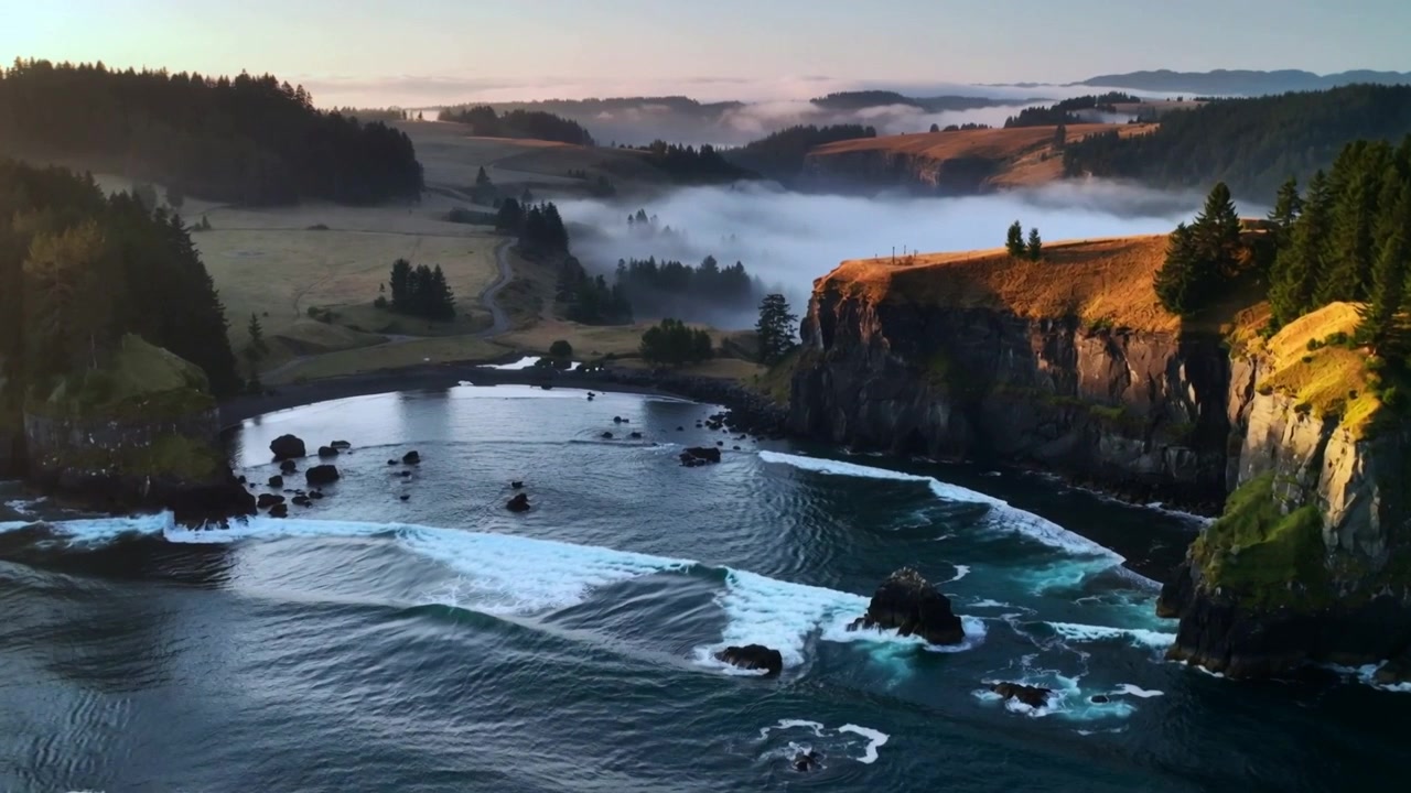 Drone che panoramica avvicinandosi alle scogliere di una baia costiera, rivelando faraglioni, la risacca e la nebbia di valle.