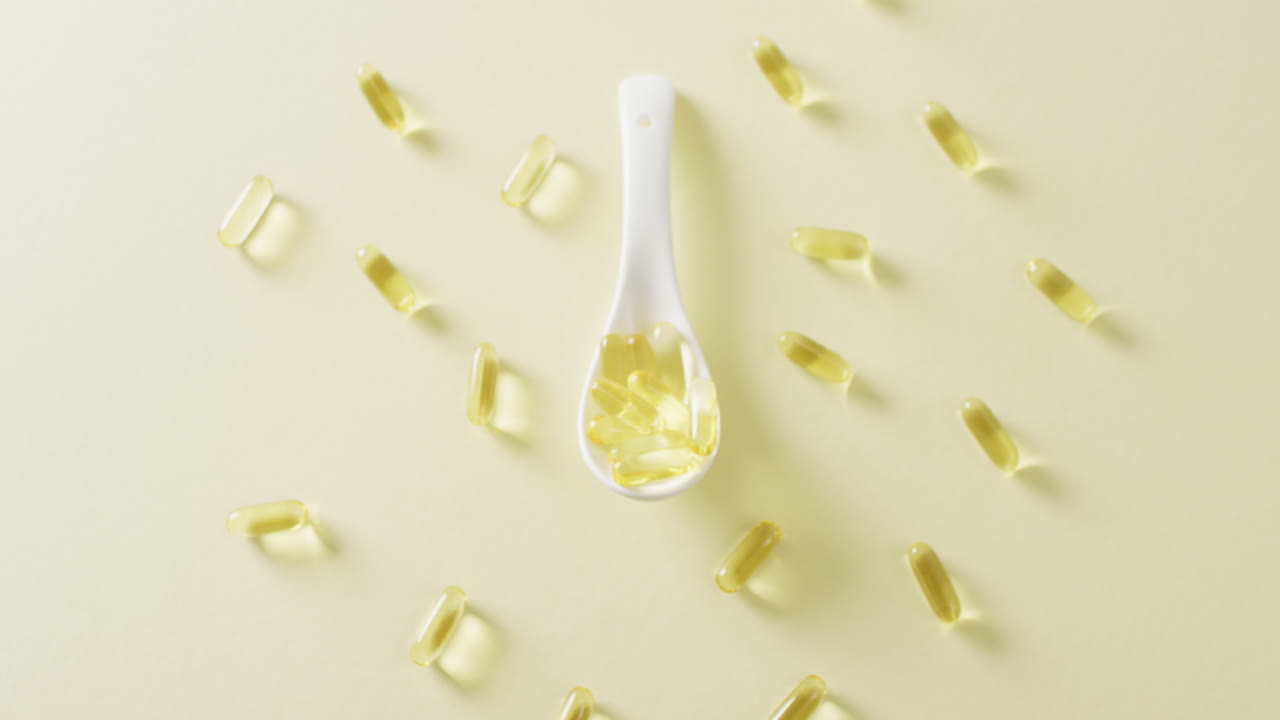 Video of oil capsules with white spoon on yellow background with copy space