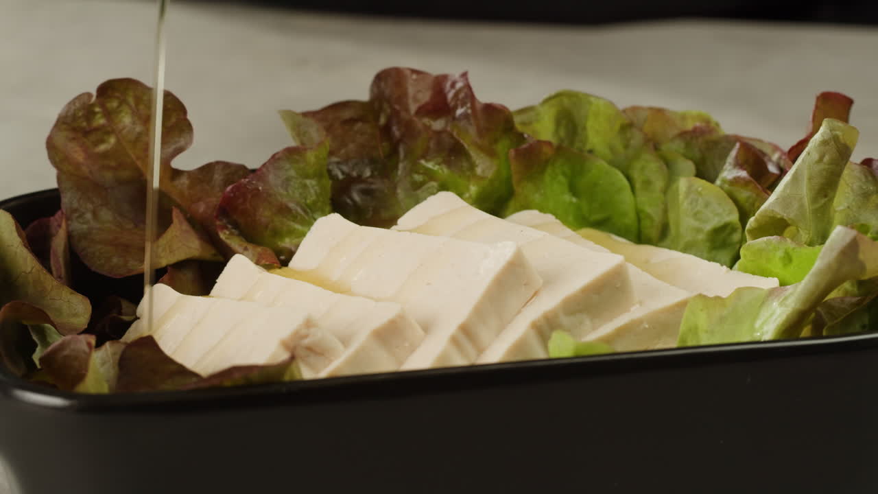 Fried tofu with sesame seeds and spices on cast iron pan, cooking japanese salad. Healthy ingredient for cooking vegan vegetarian diet food. Roasted tofu over black background.