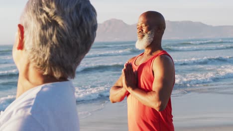 Senior-african-american-couple-practising-yoga-at-the-beach