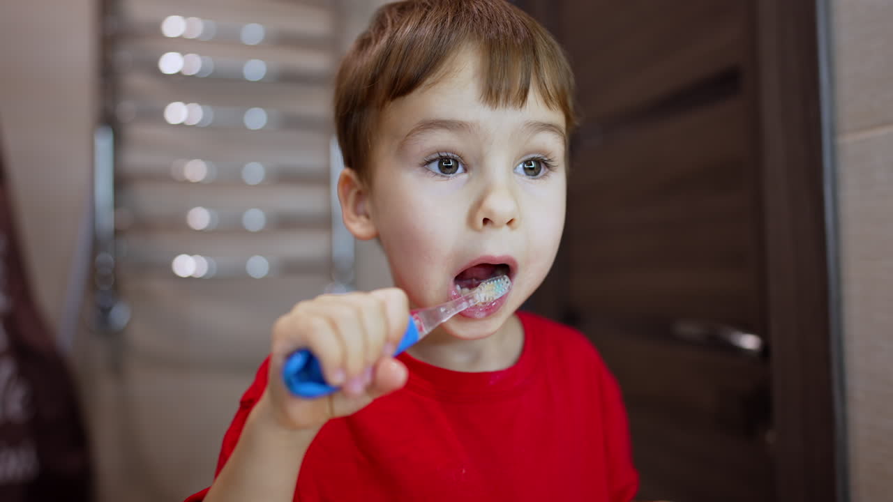 Beautiful toddler boy is cleaning teeth. Close up portrait of the kid using a toothbrush in the bathroom.