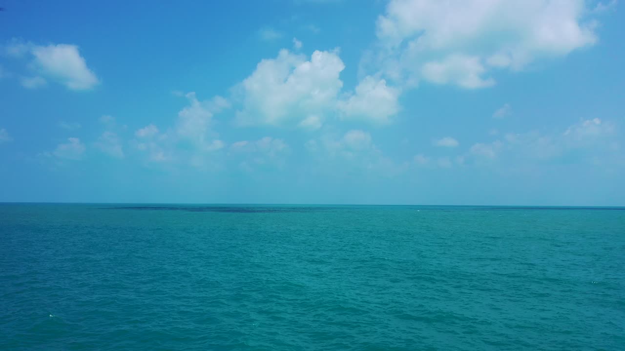 Endless calm tropical ocean with bright blue sky and fluffy clouds above. Aerial background