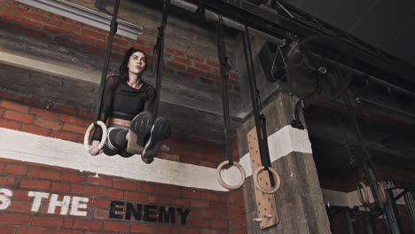 young woman performing a ring pull-up in the gym