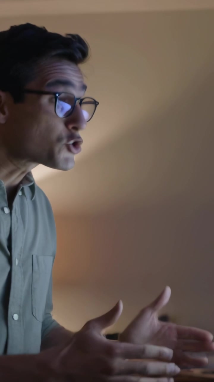 Vertical video: Pointing woman guiding man with rolled sleeves to review screen at desk, copy space