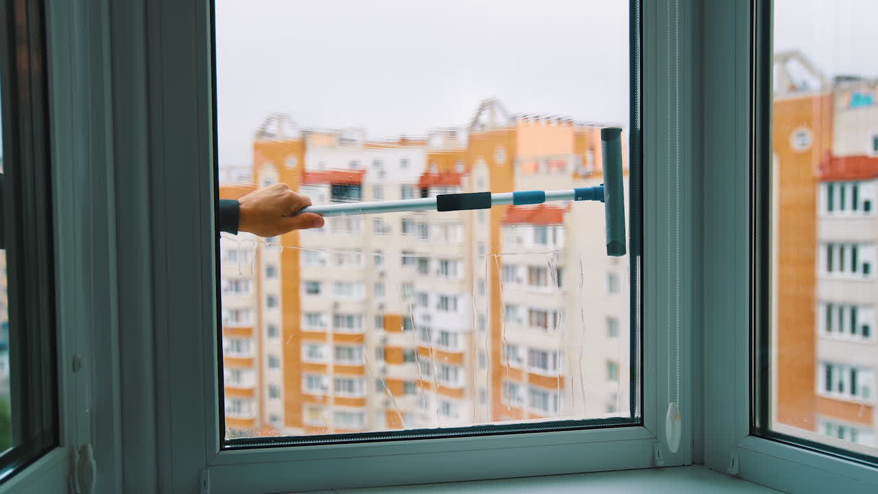 Plastic window is washing with brush. Window cleaning brush washes glass window from outside on high-rise building background.