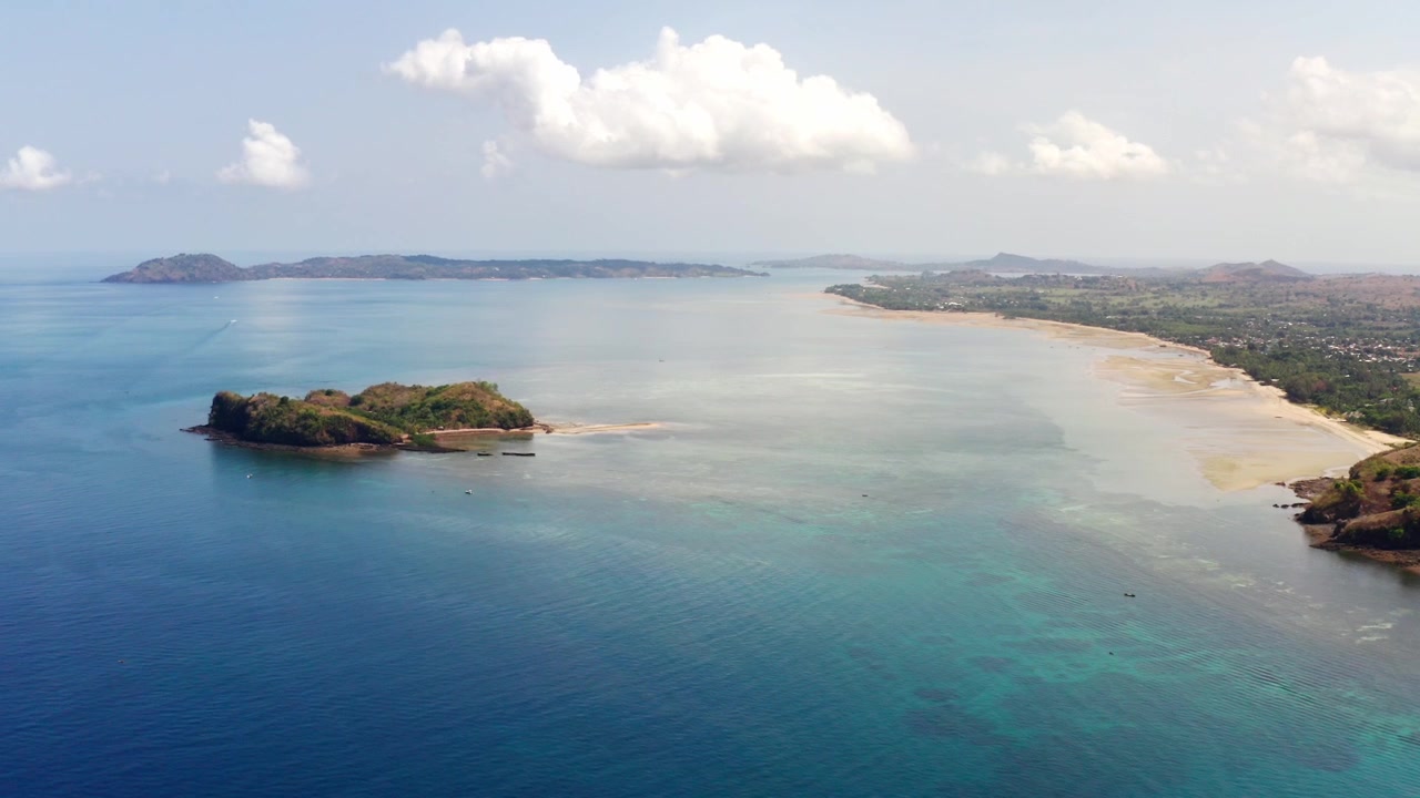 Veduta aerea con drone dell'isola di Nosy Be, Madagascar, Africa, durante una giornata di sole; l'oceano blu e la costa della spiaggia riflettono le nuvole di fronte a Dzamandzar. Nosy Tanga e Nosy Sakatia all'orizzonte.