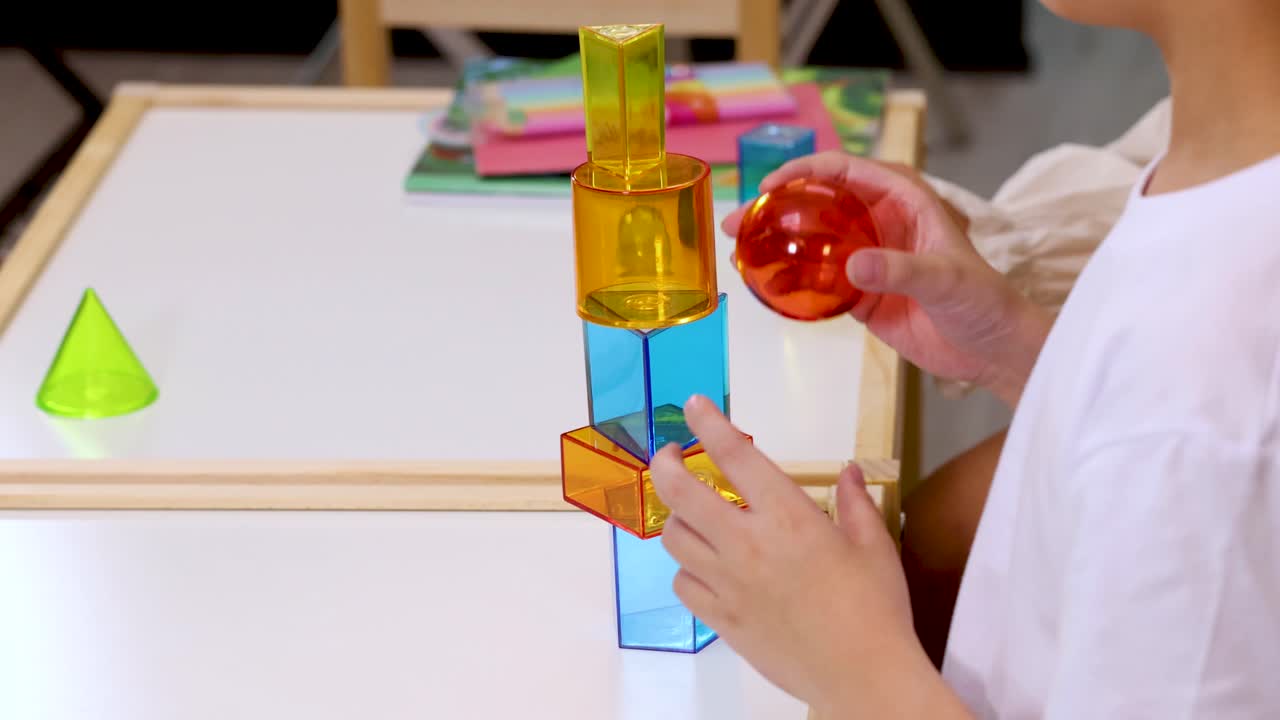 Children collaboratively stack translucent blocks on a table in a bright, creative classroom environment