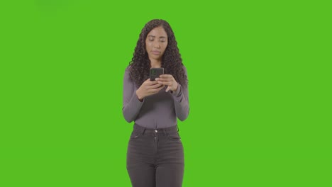 retrato de tres cuartos de longitud de mensajes de texto de mujer en teléfono móvil contra pantalla verde
