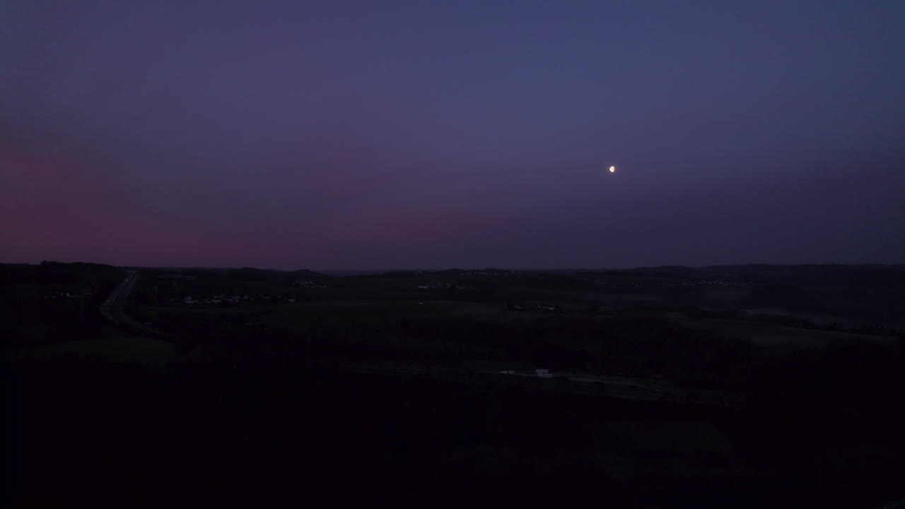 Aerial shot showing the breathtaking sight of a small, glowing moon visible in the morning's rich blue-purple sky