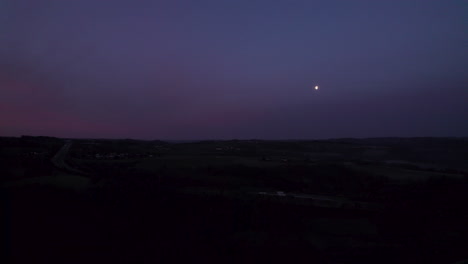 aerial shot showing the breathtaking sight of a small, glowing moon visible in the morning's rich blue-purple sky