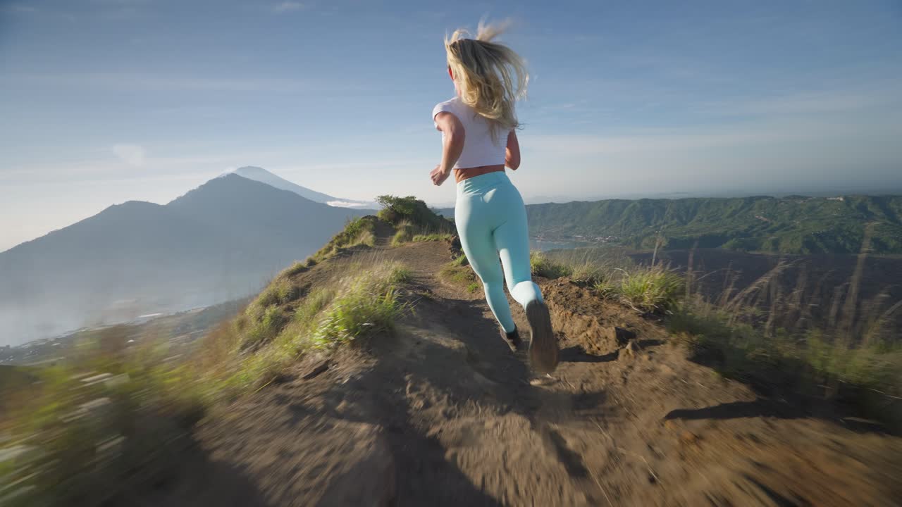 mujer rubia intrépida corriendo rápido en la cresta de la montaña de batur, alta en la vida