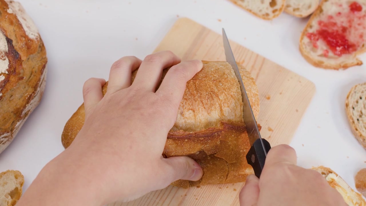 Person Slicing Fresh Loaf of Bread on Wooden Cutting Board