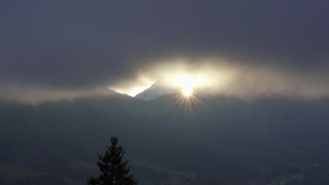 la estrella del sol brilla a través de las nubes al amanecer entre una brecha de montaña en los alpes