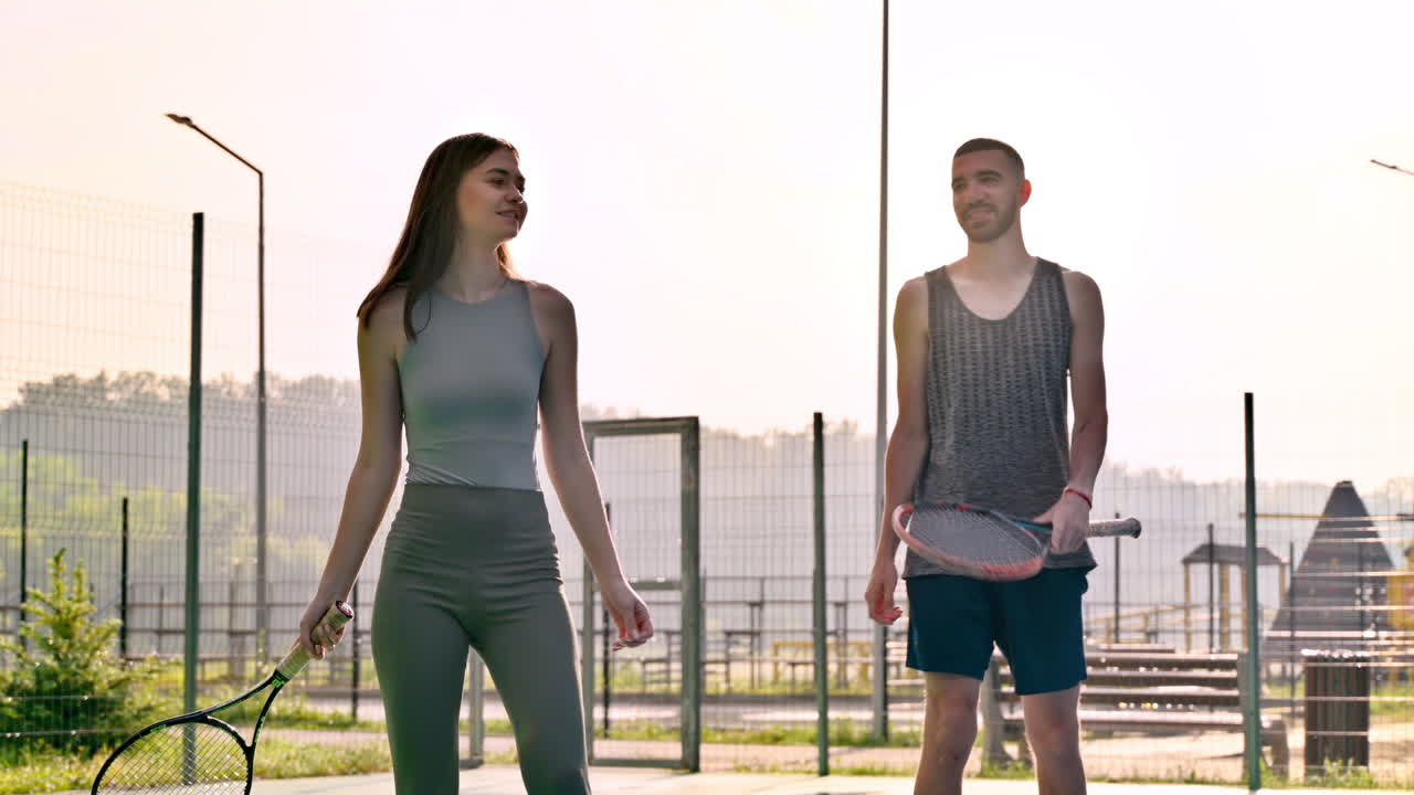 A man and a woman practicing tennis at sunset, after rain