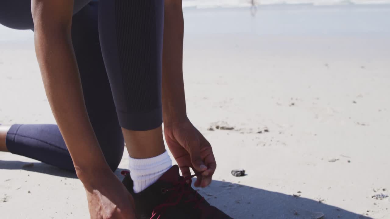 African American woman tying her shoe on the beach and blue sky background