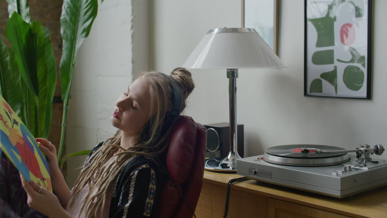Afslappet pige lytter til vinylplade med hovedtelefoner derhjemme