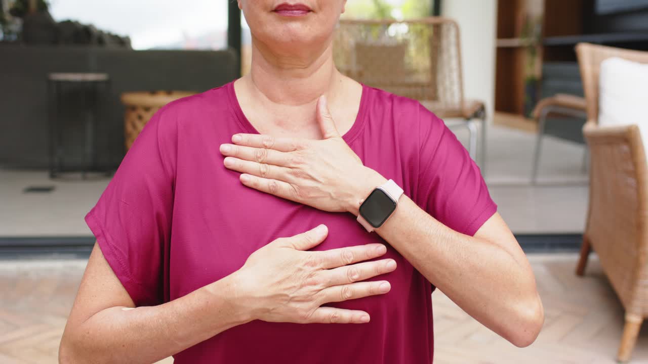 Donna che porta le mani verso l'interno in posizione di radicamento su un tappetino verde da patio, top magenta, leggings viola, smartwatch