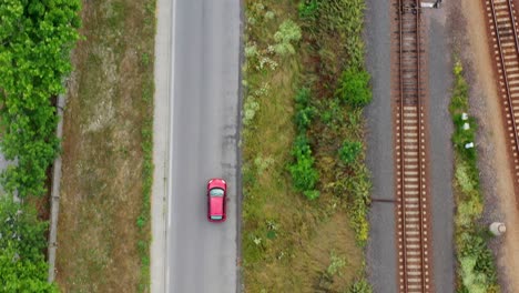 a red car driving on an asphalt road next to a railway