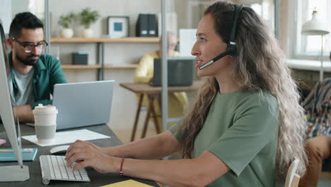 Mujer-Con-Auriculares-Hablando-En-Una-Llamada-Web-Y-Trabajando-En-Una-Computadora-En-La-Oficina