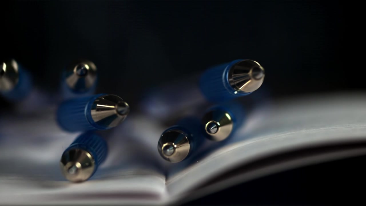 Blue Ballpoint Pens Falling onto an Open Notebook in Slow Motion