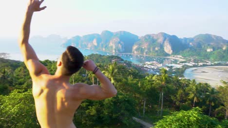 muscular man doing the zyzz pose at a lookout over the ocean phi phi island, thailand.
