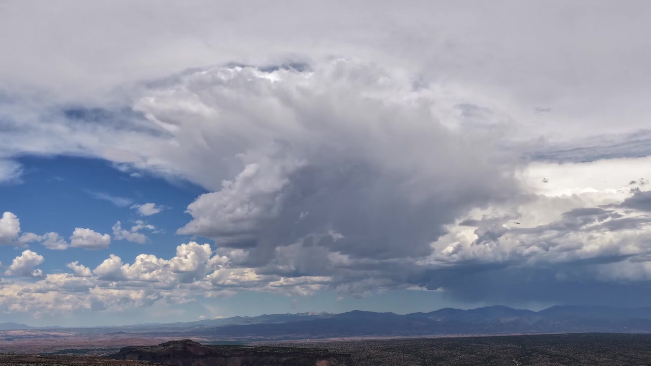 Timelapse 4K UHD con drone che mostra una splendida nuvola cumuliforme bianca brillante stagliata contro una più scura e piatta formazione nuvolosa. La massiccia formazione si trasforma rapidamente sopra un'aspra valle del Sud-Ovest
