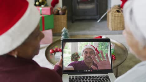 sonriendo diversas amigas mayores usando una computadora portátil para una videollamada de navidad con un hombre en la pantalla
