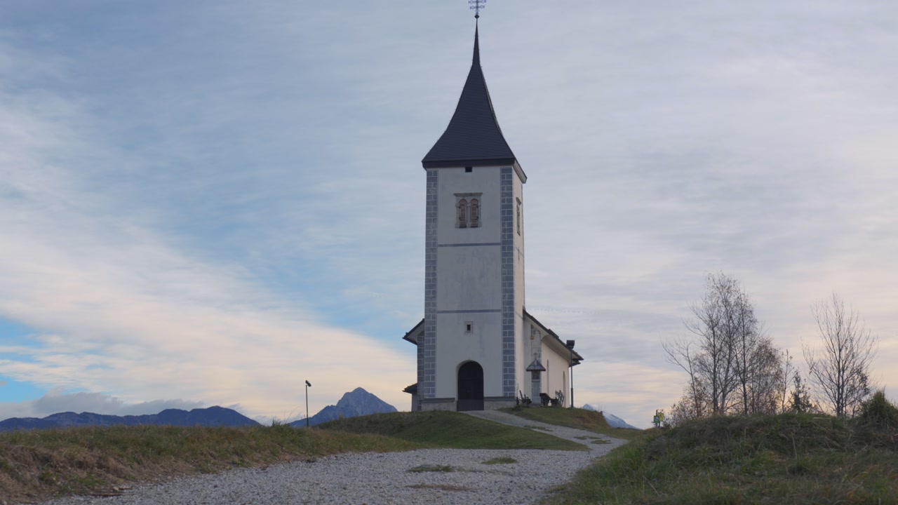 Cinematic tilt up of Jamnik church on hilltop with scenic mountain landscape in Slovenia