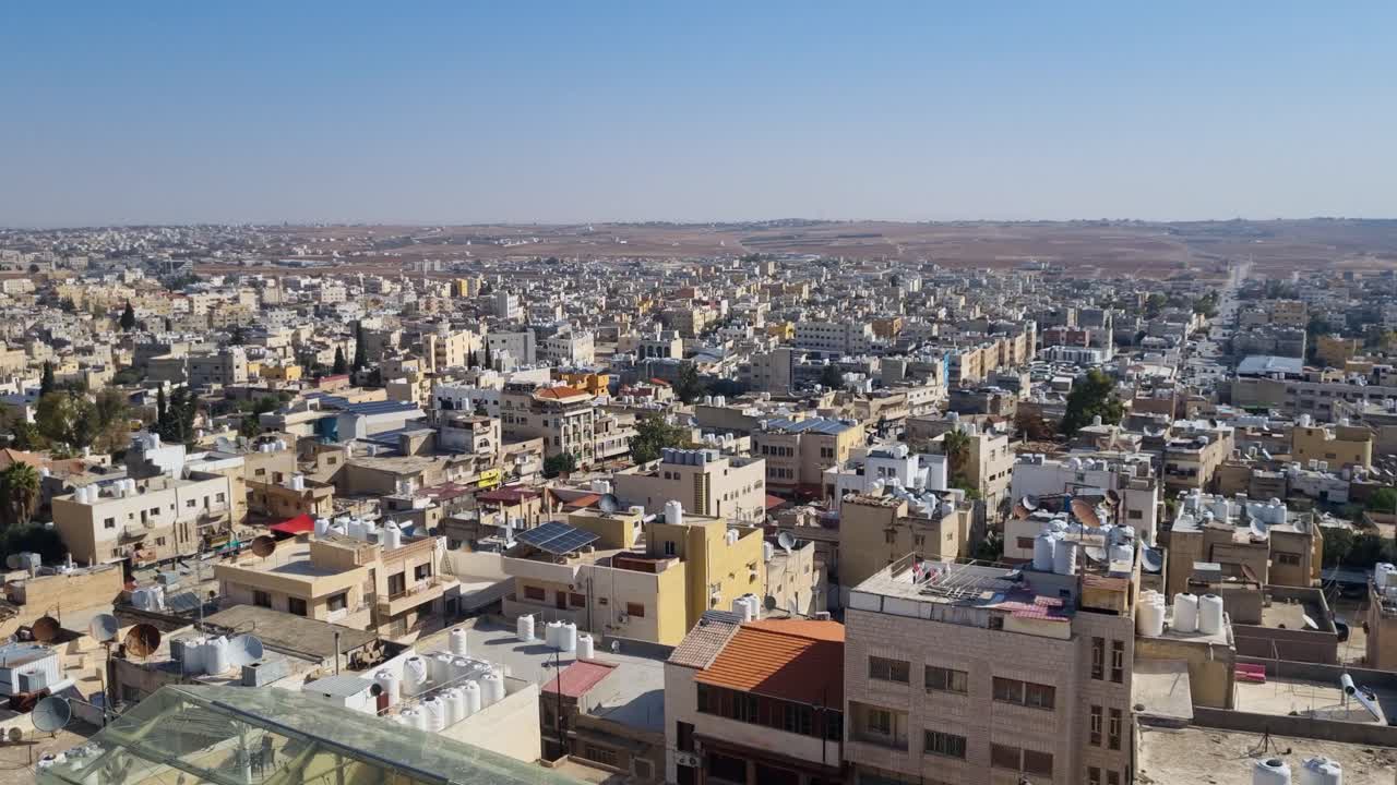 Panoramic skyline view over Madaba, Jordan, with morning sun illuminating rooftops and the city stretching across rolling hills toward the distant horizon