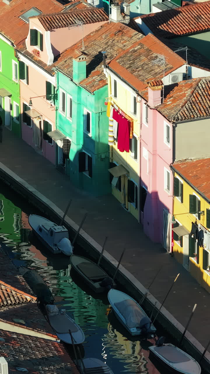 Aerial drone view of boats on the sides of a canal near the colourful houses of Burano. Vertical