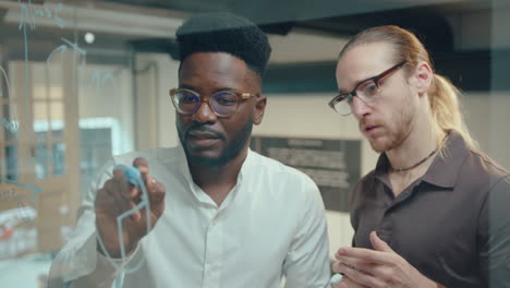 two businessmen discussing financial diagram on glass office wall