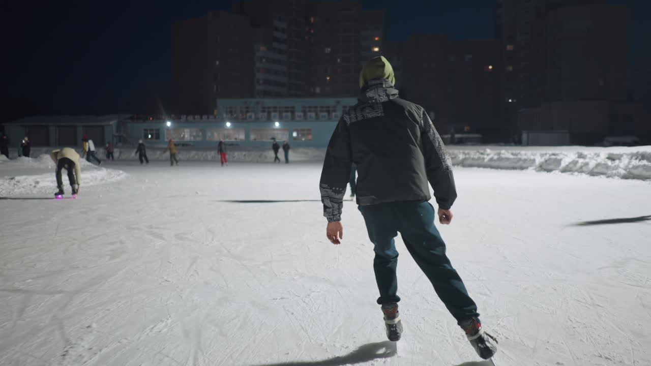 back view group of people skating on outdoor ice rink during winter night in urban area brightly lit scene shows joyful skaters wearing winter clothes with high rise buildings glowing in background