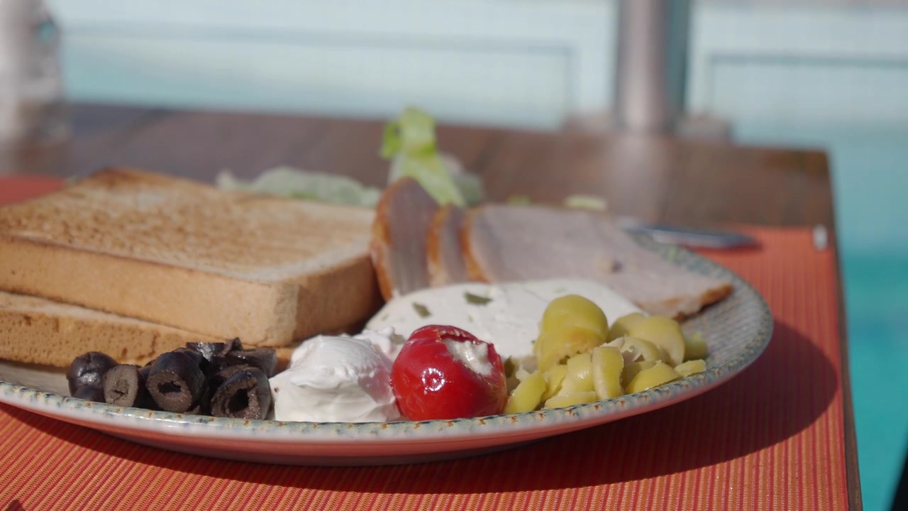 Plato de desayuno saludable con tostadas, queso y aceitunas junto a la piscina