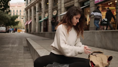 mujer sentada en la calle, tomando un lápiz rojo de su bolso