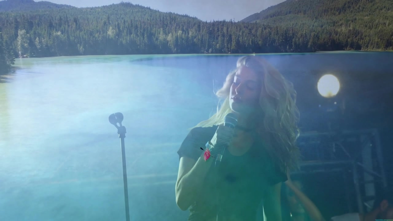 Cantante donna che si esibisce con i compagni di band sul palco, fondendo un lago con un'illuminazione a traliccio metallico per la musica.