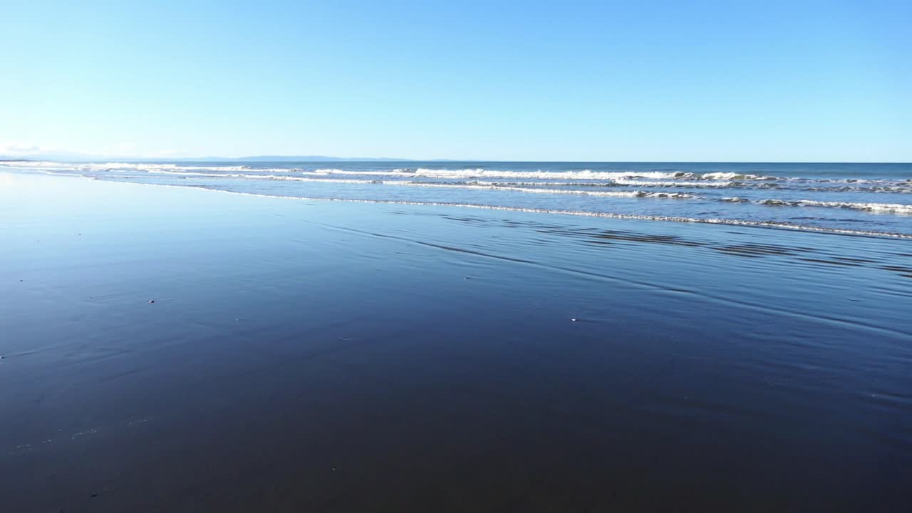 Mountain Bike riding on beach at low tide, late afternoon in winter with deep blue reflection of sky - Pegasus Bay, New Zealand