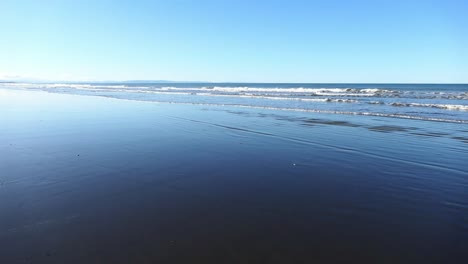 mountain bike riding on beach at low tide, late afternoon in winter with deep blue reflection of sky - pegasus bay, new zealand