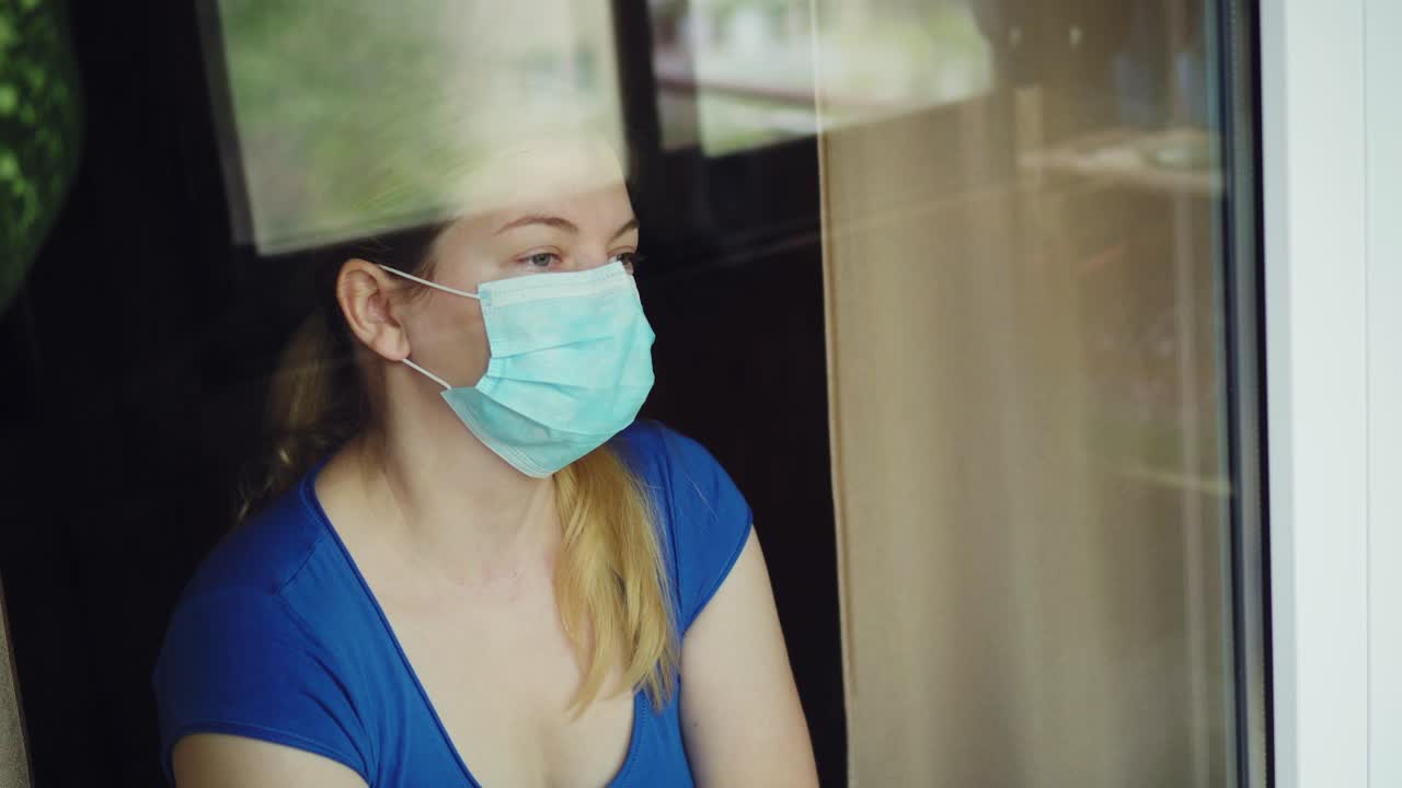 una mujer con una máscara médica mira por la ventana y habla en el móvil 02