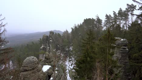 outlook-on-a-sandstone-rock-formation-in-Prachov-Rocks,-Bohemian-Paradise,-in-winter-with-flying-snowflakes,-slow-pan-left